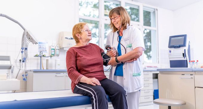 Pflegekraft misst Blutdruck einer älteren Patientin
