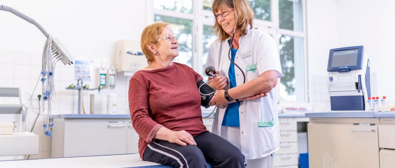 Pflegekraft misst Blutdruck einer älteren Patientin