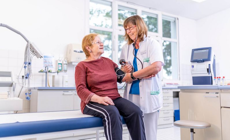 Pflegekraft misst Blutdruck einer älteren Patientin